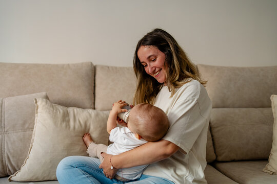 Happy mother bottle feeding baby at home