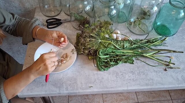 Preparing herbs and garlic for preservation in jars on a kitchen