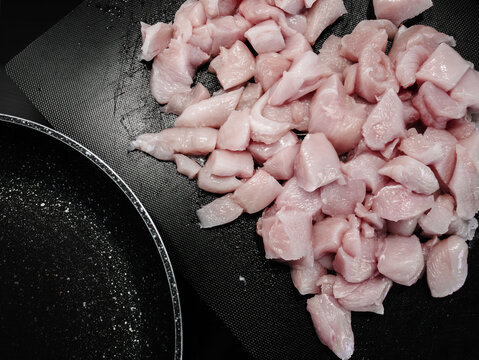 Raw chicken breast pieces on black cutting board beside frying pan