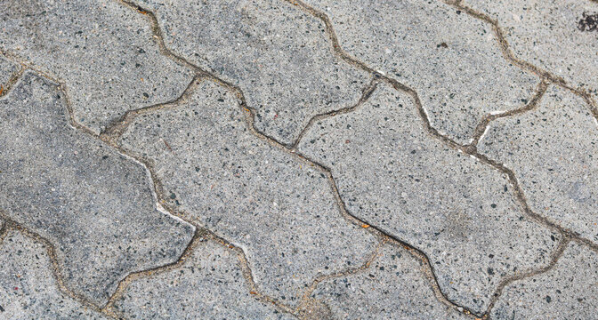 Close-up view of weathered grey interlocking paver stones with coarse aggregate textures and defined joint lines.