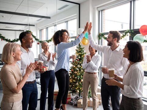 Diverse group of colleagues celebrating a successful year with high fives and festive decorations in a modern office setting.