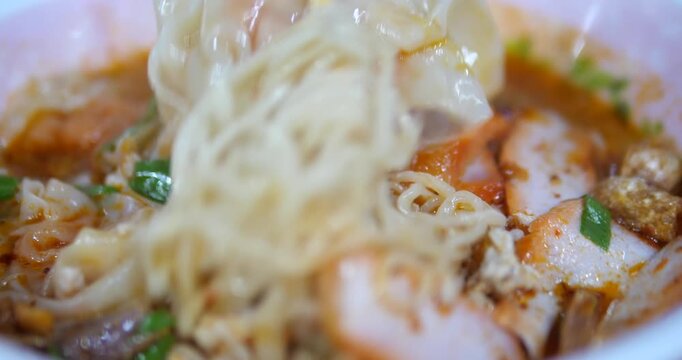 Close up of picking up yellow noodles from spicy tom yum soup
