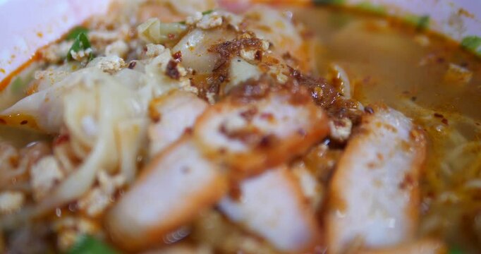 Close up of sliced BBQ pork in spicy tom yum noodle soup
