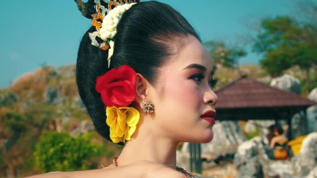 A focused portrait of a female performer in traditional costume maintaining eye contact while positioning her hand in a dance mudra near her face.