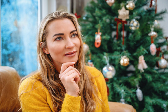 Woman thinking while seated next to a decorated Christmas tree in a