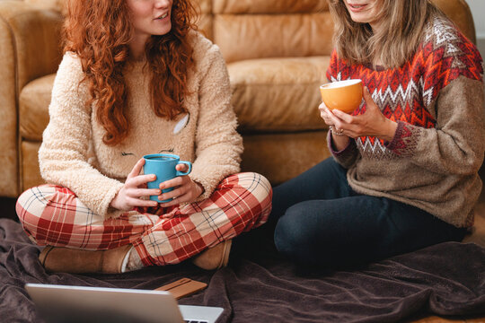 Two friends sit on a couch, chatting and drinking warm drinks on a
