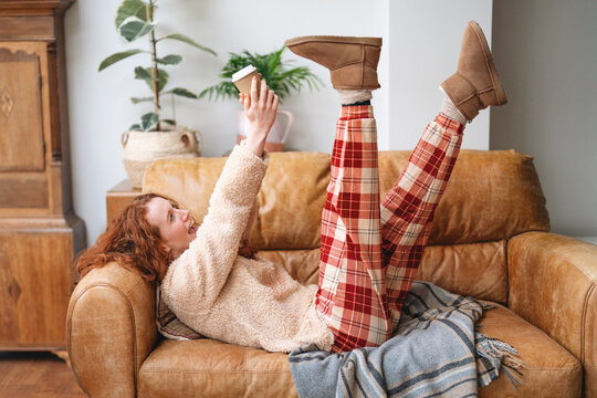Woman relaxing on a couch while enjoying a drink and wearing cozy