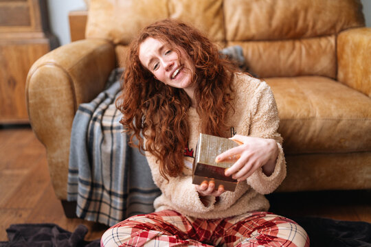 Person sits on floor and enjoys opening a gift in a cozy living room