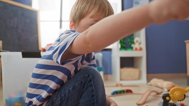 Boy sitting, hands pressing buttons on a toy cash register while playing in an indoor playroom building; concentration.