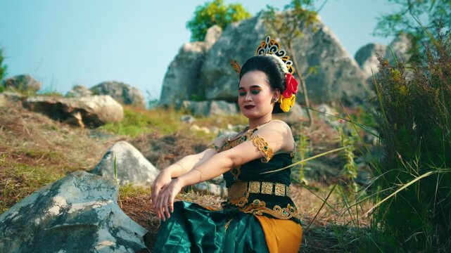 A medium shot capturing an elegant and slightly alluring pose of a traditional dancer sitting in nature, gently touching her shoulder and neck.