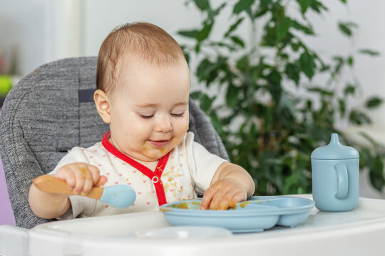 Baby girl eating with spoon and messy face in high chair
