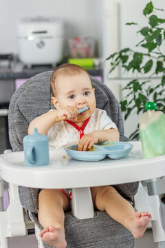 Baby eating with spoon in mouth in high chair