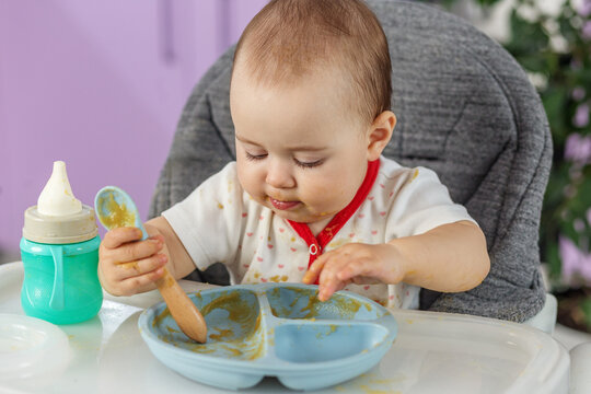Baby eating puree with spoon in high chair close-up