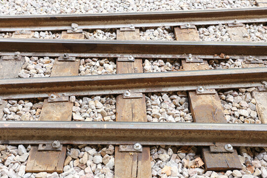 Railway tracks with wooden sleepers and gravel. Parallel steel rails and weathered timber ties. Railroad infrastructure background. Close detail of old train route construction and track fasteners.