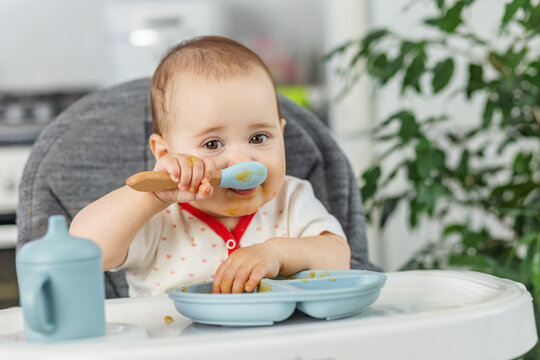 Baby eating puree with spoon close-up in high chair