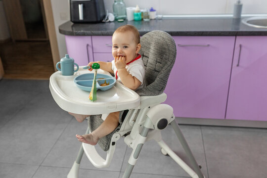 Happy baby eating finger food in high chair side view