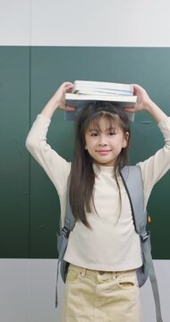 Playful schoolgirl balancing a stack of books on top of her head with a happy smile.