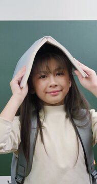 Playful student girl wearing a book on her head and making funny expressions.	