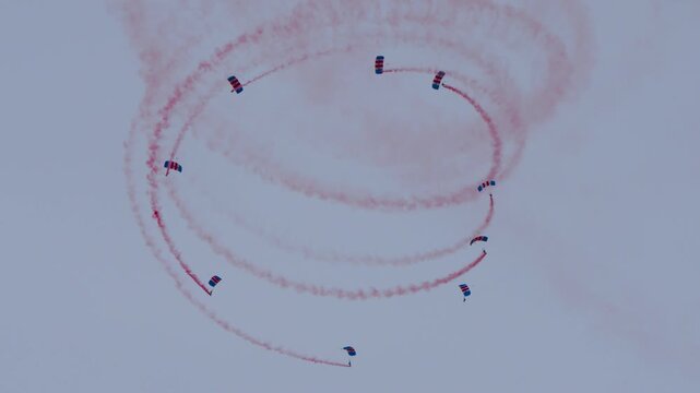 Parachute team falling in a circle formation with red smoke trails