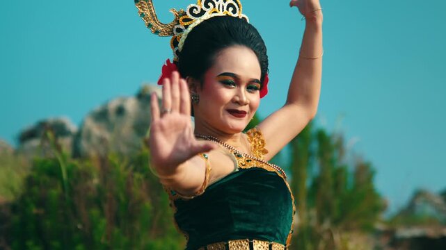 Dramatic close-up of a female dancer raising her hand high, possibly to shield her eyes from the sun or as part of a traditional dance choreography.