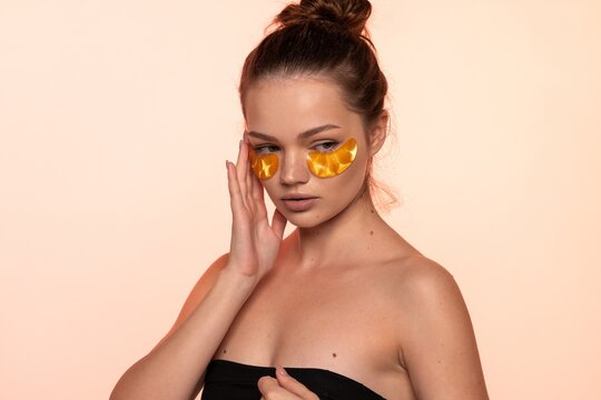 Young woman applying golden eye patches for under-eye care, focusing on beauty ritual and skincare hydration