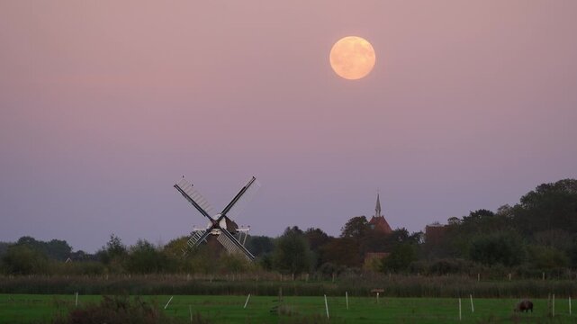 Full moon over a traditional windmill in the Dutch countryside. Groningen, the Netherlands.