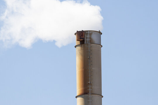 Factory chimney emitting white smoke into blue sky