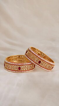 Elegant gold bangles with red accents displayed on a soft background  