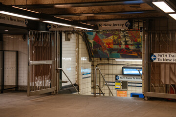 Fototapeta premium New York City, New York, USA - 08.05.2024: Interior corridor of a subway station with directional signs pointing to PATH trains to New Jersey. Underground transportation passage connects commuters