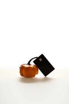 Black Credit Card and Small Autumn Pumpkin on White Background for Seasonal Shopping Concept