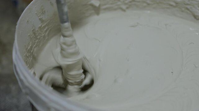 Plaster mixture being stirred with mixing paddle in bucket