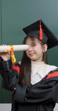 Cute Asian girl looking through rolled diploma paper like a telescope for educational future vision.