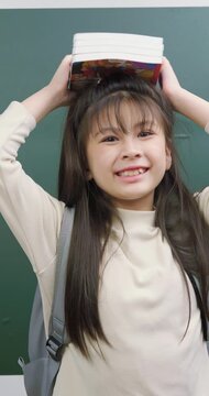 Playful schoolgirl balancing a stack of books on top of her head with a happy smile.