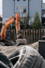 Orange excavator with bucket at an urban residential construction site, surrounded by gravel © Natalia Schuchardt