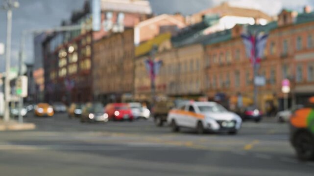 A blurred busy urban intersection shows multiple vehicles on the road, including cars and taxis. Surrounding buildings display different colors, with city life evident in an afternoon setting