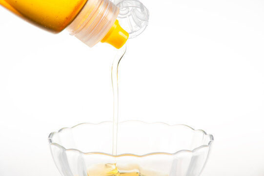 Golden Natural Honey Dripping from Squeeze Bottle into Clear Glass Bowl on Pure White Background