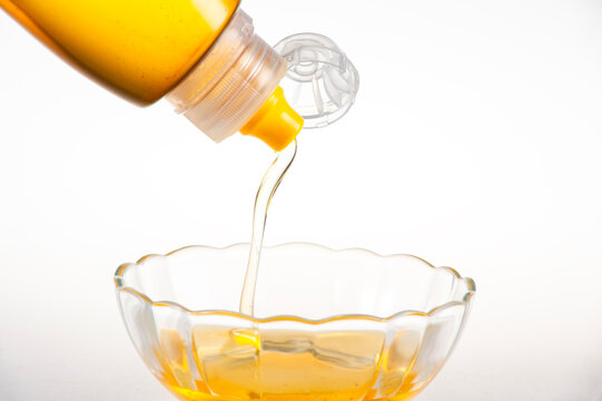 Golden Natural Honey Dripping from Squeeze Bottle into Clear Glass Bowl on Pure White Background