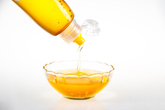 Golden Natural Honey Dripping from Squeeze Bottle into Clear Glass Bowl on Pure White Background