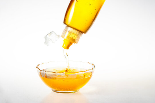 Golden Natural Honey Dripping from Squeeze Bottle into Clear Glass Bowl on Pure White Background