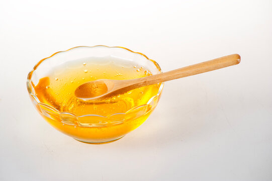 Golden Raw Honey in Scalloped Glass Bowl with Wooden Spoon on Pure White Background