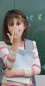 A cheerful schoolgirl twirls a pencil in her hand. She smiles in a classroom.