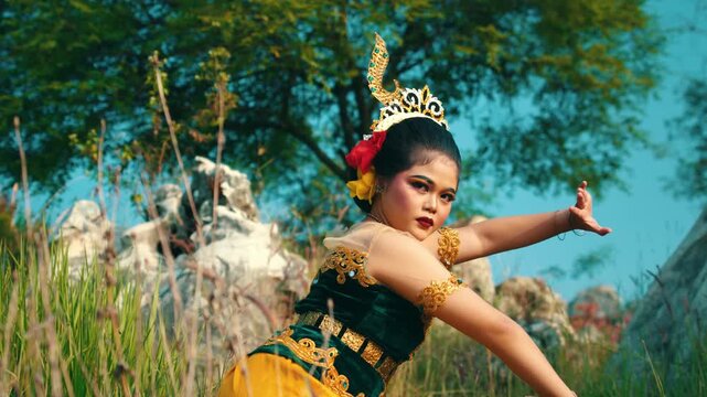 Footage of a female dancer executing a low crouching dance movement with graceful arm gestures in a grassy field.