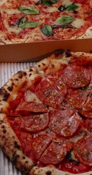Two open delivery boxes featuring Margherita and spicy salami pizzas side-by-side on a wooden table.
