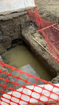 Construction worker demonstrates excavated pt with water main pipe and sewer pipeline laid in soil profile