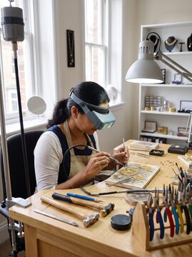 Female Jeweler Using Magnifying Visor to Craft Handmade Gold Jewelry