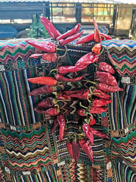 Bright red chili peppers hanging on colorful traditional patterned textile. Dried spicy vegetables displayed at outdoor market bazaar. Ethnic culture, agriculture, and traditional cuisine concept.