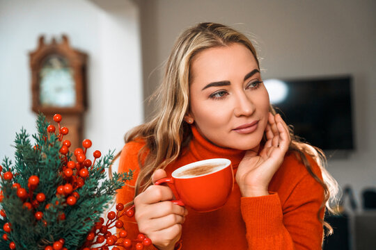 Woman sitting inside a room holding a red cup and looking thoughtful