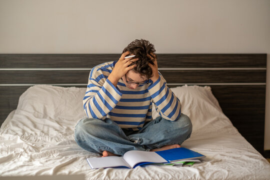Teenage boy holding head above hard school assignment, evening spent over single page, story told without any single spoken word. Wide shot. Concept of school assignment done without any help