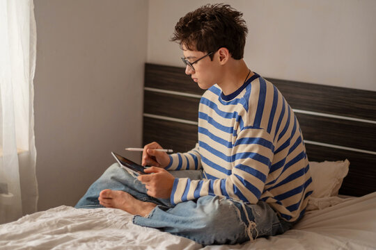 Teenage boy holding tablet and digital pen at home, sketch made with thin digital pen, moment impossible to repeat on second day. Wide shot. Concept of digital drawing on tablet at home