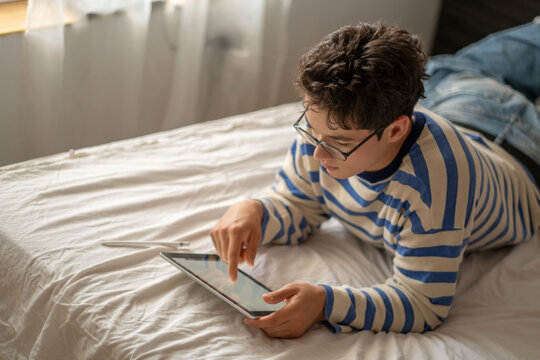 Teenage boy holding tablet and digital pen at home, sketch made with thin digital pen, detail that turns ordinary hour into content. Wide shot. Concept of digital drawing on tablet at home